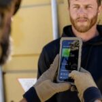 Gloved hands hold a smartphone displaying a biometric authentication screen during a security check.
