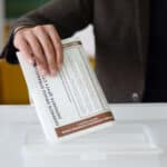 Person places a folded newspaper into a white office printer tray, holding it with fingers.