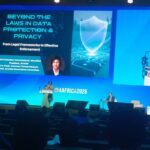 Speaker at a podium on a blue-lit stage, large screen behind reading 'Beyond the Laws in Data Protection & Privacy' with ID4AFRICA 2026 branding.
