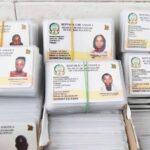 Stacks of Angolan national ID cards bound with rubber bands, each with a photo and text 'República de Angola Bilhete de Identidade Nacional'