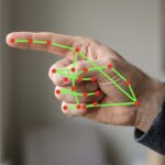 Close-up of a hand with a green skeletal overlay of red joints, showing a hand-tracking gesture.