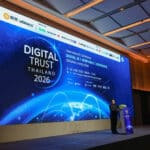 Conference stage with large blue Digital Trust Thailand 2026 banner and speaker at podium, sponsor logos along top edge