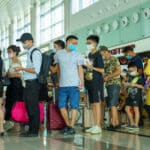 Group of travelers wearing masks with rolling suitcases in a bright airport/terminal.