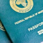 Close-up of a blue passport cover with gold embossed seal and the text 'Federal Republic of Nigeria' visible along the edge.