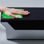 Hand tapping a green card on a black contactless payment terminal, indicating a contactless payment.